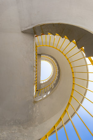 Bottom view of a concrete spiral staircase with yellow railings on a sunny morningの写真素材