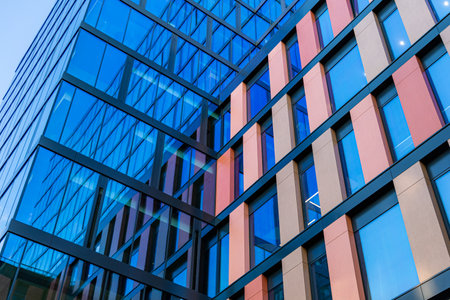 Wroclaw, Poland - June 2022: Upward view of a tall and modern office building full of glass windows reflecting the walls, decorations and blue blue skyのeditorial素材