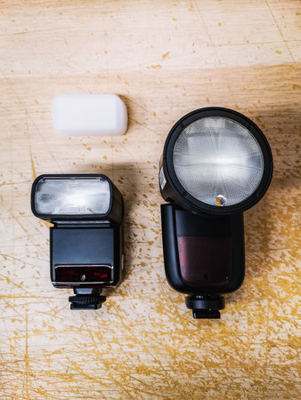 A classic, small photo reporter lamp with a diffuser next to a contemporary, large lamp with a round...
