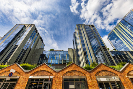 Warsaw, Poland - July 2022: Tall glass corporate buildings facing a small brick arcade of small shopsのeditorial素材