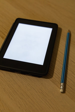 Blue pencil lying on a small wooden table next to a small ebook reader which looks like a tabletの写真素材