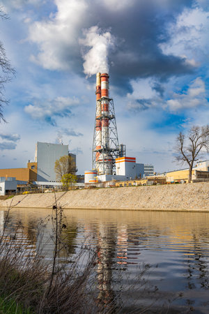 Wroclaw, Poland - April 15 2023: High white and red industrial smoking chimneys reflecting in water of Odra river at sunny cloudy dayのeditorial素材