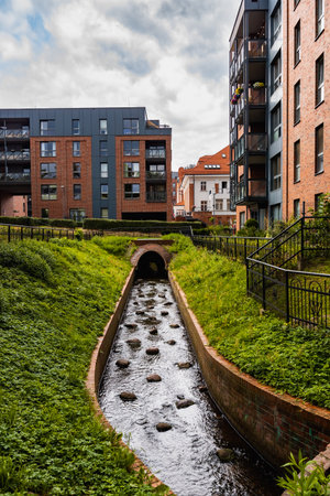 Gdansk, Poland - July 23 2023: Small water stream with few decorative stones inside next to modern...