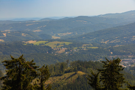 Beautiful green and blue panorama of layers of mountains and trees and some fields seen from top of viewing tower at highest mountain in this areaの写真素材