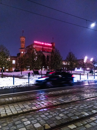 Wroclaw, Poland - December 7 2023: Beautiful and colorfully glowing light stripes of tram and cars at tram station next to main railway station with big and glowing neon lamp on topのeditorial素材