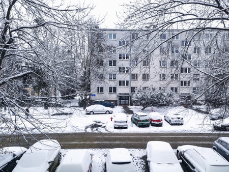 Wroclaw, Poland - December 2 2023: Beautiful winter view through the window to city street between high old trees and cars covered with fresh white snow reflecting in small black plastic boxのeditorial素材