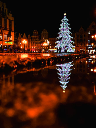 Wroclaw, Poland - December 4 2023: Beautiful and colorful Wroclaw market square with high and glowing high christmas tree reflecting in small puddleのeditorial素材