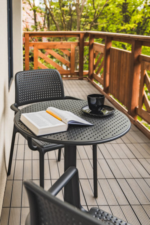 Open Holy Bible with yellow pen lying on plastic garden table with black coffee cup standing on...