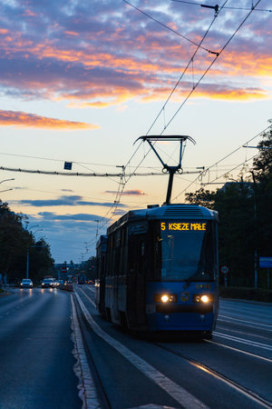 Wroclaw, Poland - October 1 2025: Urban street with tram tracks and passing trams illuminated by sunset light, capturing evening city traffic, overhead cables, and vibrant sky colorsのeditorial素材
