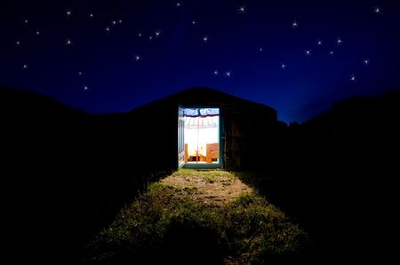 there is light from the open door of yurta house standing against night dark blue sky with starsの写真素材