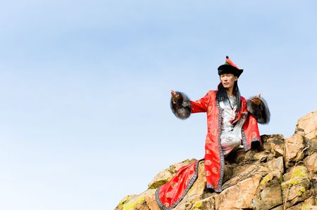 young asian man in fine Mongolian suit sits on rock