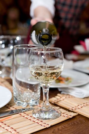 glass stemware being filled with white wine from bottle in waiters hand in restaurantの写真素材
