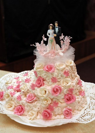 a wedding cake with pink and white flowers and a statuette on topの写真素材