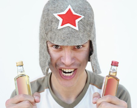 a young man in a Budenny cap holds alcohol drinks in both handsの写真素材