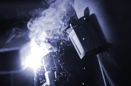 a welder in a safety mask welds, blue toning