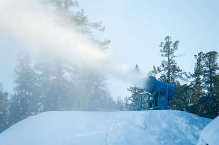 a snow gun makes snow at a hill top  at a ski resort 