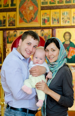 young man and woman hold their baby, at orthodox churchの写真素材