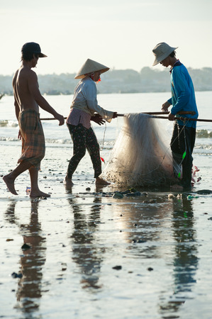 MUI NE, VIETNAM - FEBRUARY 27, 2013  Three unidentified Vietnamese fishers fold a net at the shore  Fishing is one of the principal sources of income for local people のeditorial素材