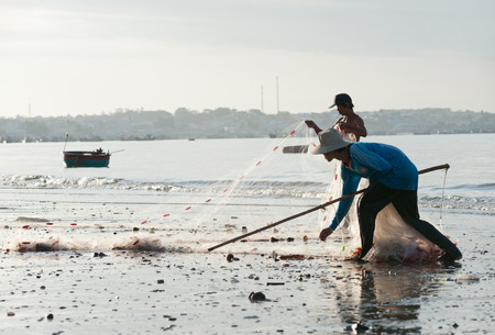 MUI NE, VIETNAM - FEBRUARY 27, 2013  Two unidentified Vietnamese fishermen fold a net at the shore  Fishing is one of the most important sources of income for local people のeditorial素材