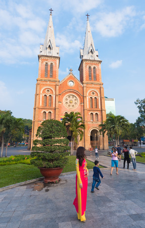 HO CHI MINH, VIETNAM - FEB 18, 2015: Saigon Notre Dame Basilica facade on Tet Eve (Lunar New Year). An unidentified young woman wears a festive national dress in Tet colours - red and yellow.のeditorial素材
