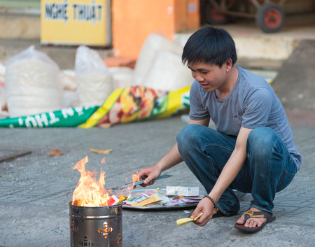 HO CHI MINH, VIETNAM - FEB 17, 2015: An unidentified man burns votive offerings by his house on Tet Eve. Many Vietnamese practice the custom of burning votive objects for religious purposes mainly.のeditorial素材