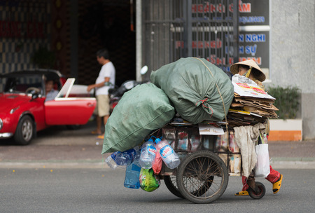 VUNG TAU, VIETNAM - JUNE 10, 2015: An unidentified senior dustwoman rolls a cart with different kinds of sorted waste for recycling. Waste selling for recycling is popular business in Vietnam.のeditorial素材