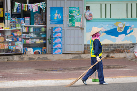 VUNG TAU, VIETNAM - JUNE 10, 2015: An unidentified dustwoman carries a broom and a dustpan along the road. Due to the climate disposition of garbage is made several times a day.のeditorial素材