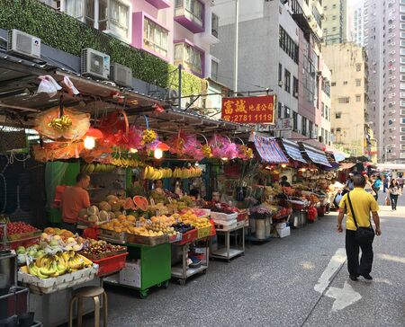 HONG KONG - SEPTEMBER 19, 2017: People walk by a line of small fruit and food shops of an outdoor wet market in Mong Kok district.のeditorial素材