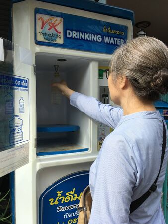 BANGKOK - SEPTEMBER 9, 2019: A middle aged asian woman fills a bottle with water at a water vending machine. There are a lot of such coin operated machines around the city.のeditorial素材