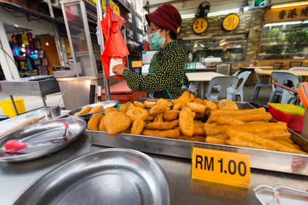 KUALA LUMPUR - MAR 13, 2017: An unidentified senior woman sells traditional chinese deep fried dough buns in Jalan Alor street famous with budget restaurants of various cuisines.のeditorial素材