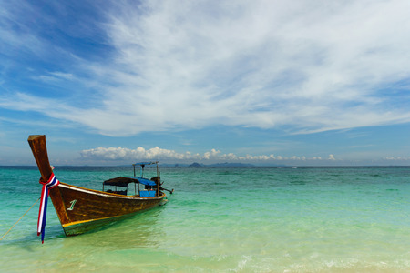Small Thai fisherman boat with Thai flag on a clear blue sea and bright sky in Phuketの写真素材