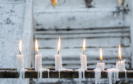 Row of burning candles with white temple wall as backgroundの写真素材