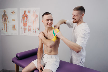 kinesiology - physiotherapist taping injured patient shoulder with kinesio tape after muscle injury
