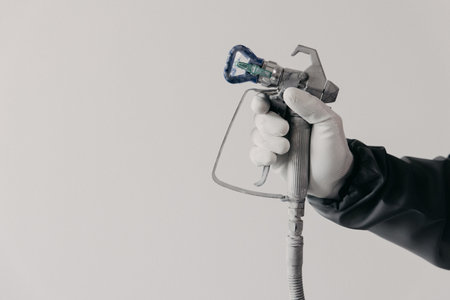A painter's arm and hand in safety coveralls and gloves holding an Industrial size airless spray gun used for industrial painting and coating. Shot on white background. high quality photoの写真素材