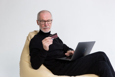 Concentrated middle aged man in eyeglasses holding credit bank card, satisfied with secure money transfer.の写真素材