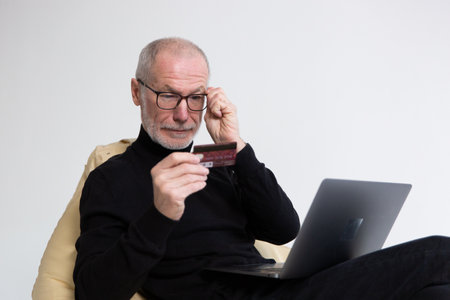 Concentrated middle aged man in eyeglasses holding credit bank card, satisfied with secure money transfer.の写真素材