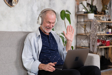 Smiling senior man wear earphones wave to camera having video call on laptop.の写真素材