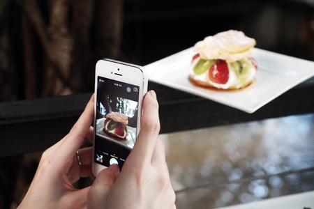 Hand holding smartphone taking picture of fruit pastry