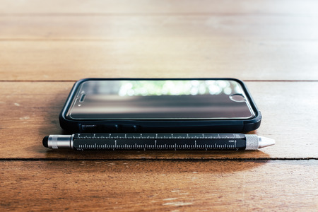 Close up mobile phone and pen stylish on wooden table, film look styleの写真素材