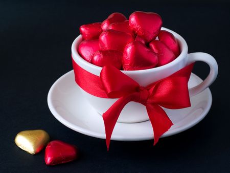 White cup with saucer with red and gold chocolate hearts and red ribbon. Photo on a black backgroundの写真素材