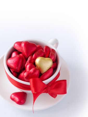White cup with saucer with red and gold chocolate hearts and red ribbon. Photo on a white backgroundの写真素材