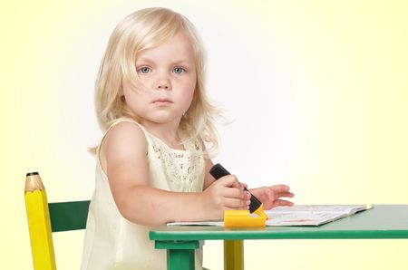 The girl sits at a table and paints the book a felt-tip pen      の写真素材