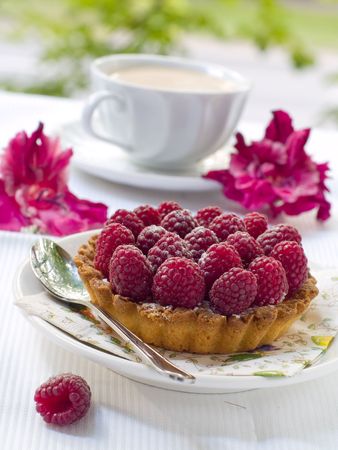 A fresh raspberry tart on a plate and cup of coffee in backgroundの写真素材