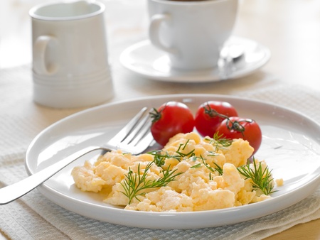 A plate of creamy scrambled eggs garnished with dill, a cup of coffe with milkの写真素材