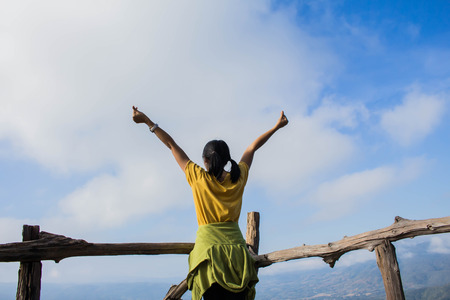 Young Woman standing alone outdoor with wild forest mountains on background Travel Lifestyle and survival concept rear view, Woman spreading hands with joy and inspiration in mountains.の写真素材
