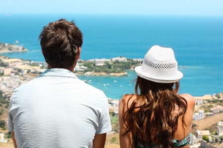 Picture of a young couple sitting side by side and looking at the blue sea.の写真素材