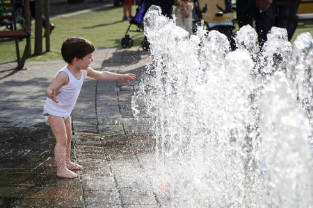 Little cute boy playing with the water from the fountainの写真素材