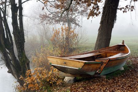 Misty autumn morning by the river with damaged rowboat.の写真素材