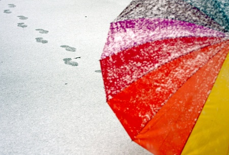 Colorful umbrella in the fresh snow with some footprints around it.の写真素材