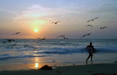Surfer runing on the beach with sunset in the background.